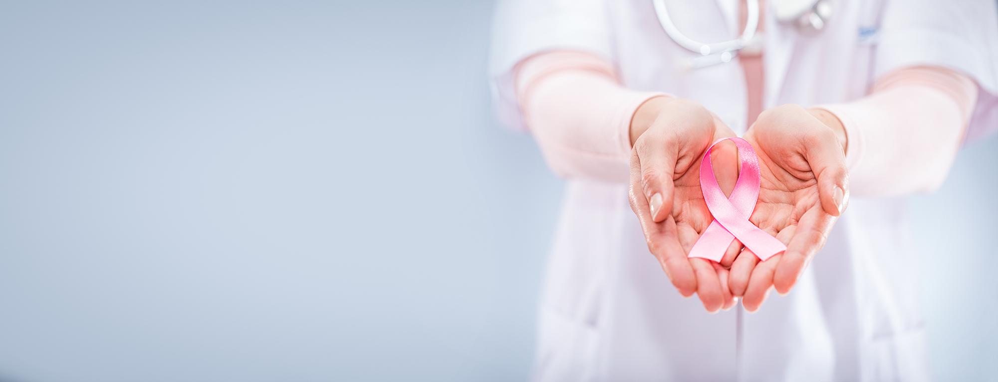 A clinician in a white coat holding a pink breast cancer awareness ribbon in cupped hands