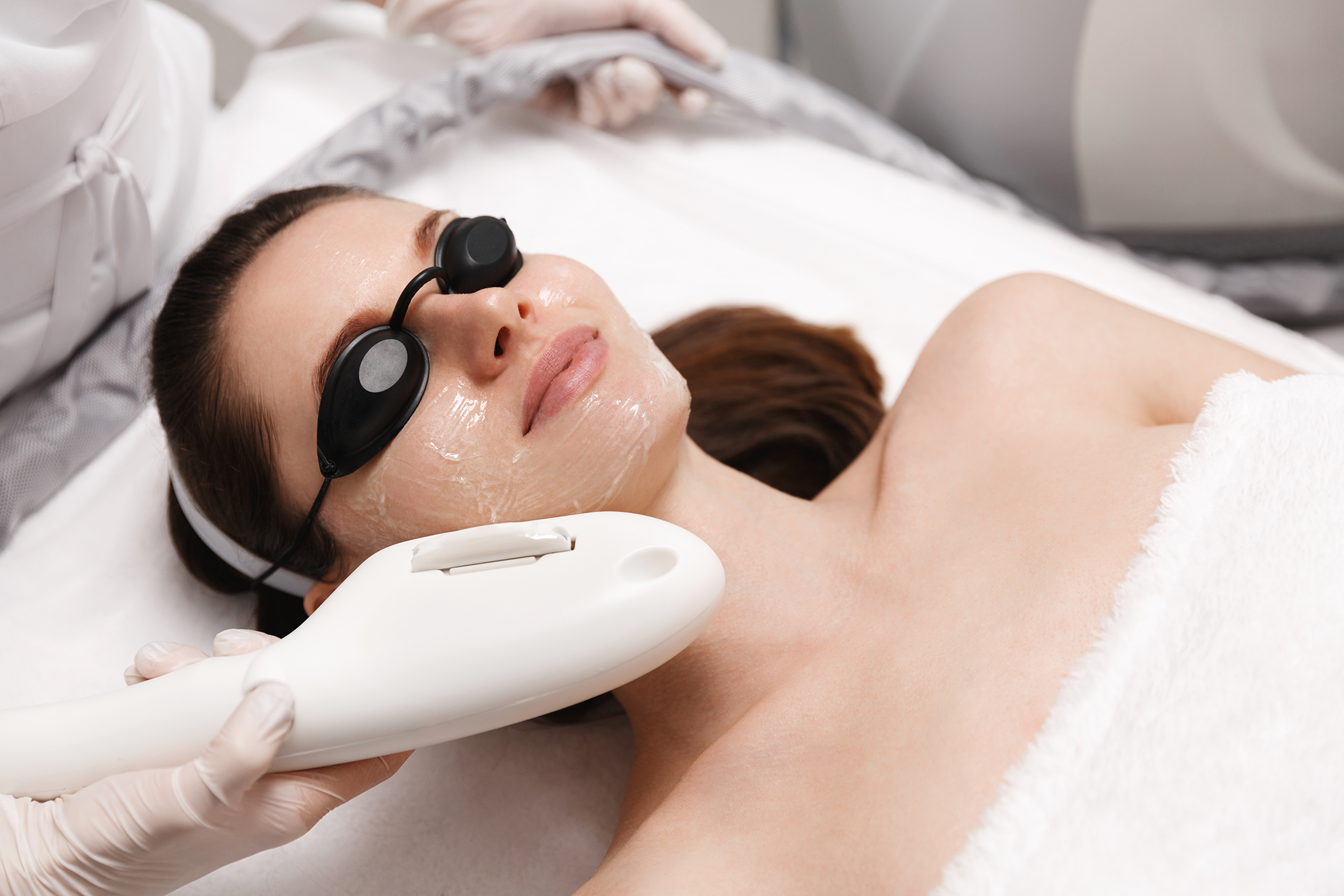 Client in protective eyewear receiving a laser treatment with a cooled handpiece at Laser Me in St. Louis